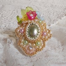 Bague Envolée Fleurie brodée avec un cabochon ovale Olivine en résine, ornée de perles rondes nacrées, des rocailles, fleurs Lucites, mini gouttes, chaton en Cristal et perles rondes aplaties.